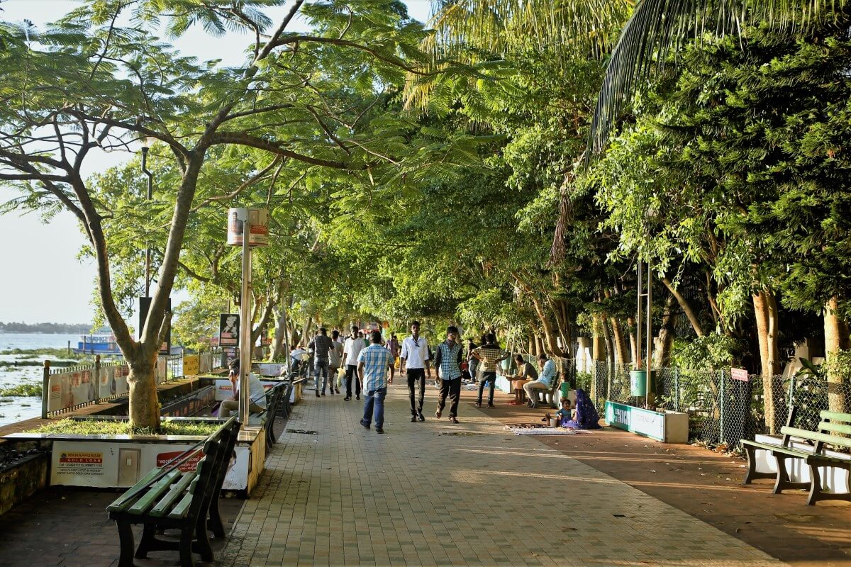 Uma fotografia da Marine Drive em Kochi; pessoas caminham sob a cobertura de árvores.