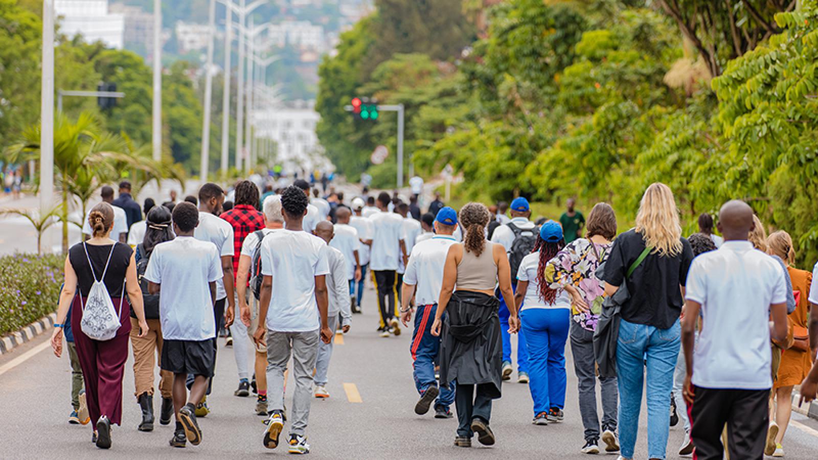 Um grupo de pessoas caminhando por uma rua arborizada e sem carros em Kigali
