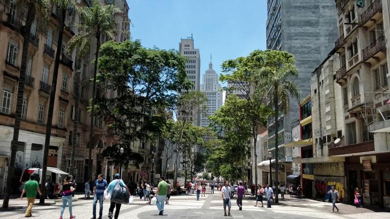 Pessoas andando por uma rua urbana ladeada de árvores.