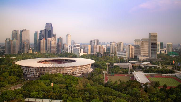 Vista do Estádio Gelora Bung Karno, em Jacarta, cercado por árvores e pelo horizonte da cidade