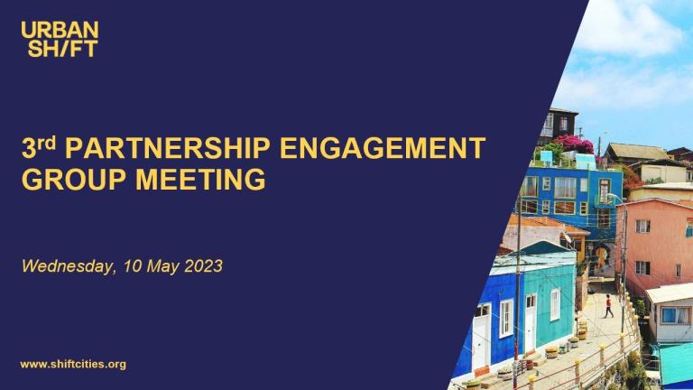 um slide onde se lê 3ª reunião do grupo de engajamento de parceria contra um fundo azul-marinho; uma imagem de edifícios coloridos à direita