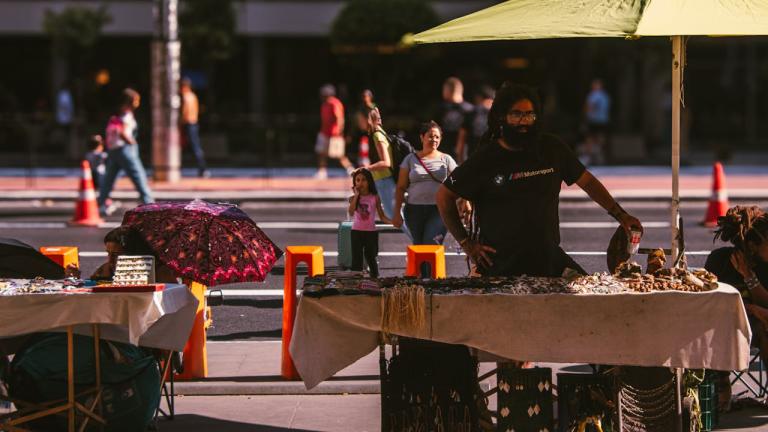 um vendedor ambulante fica sob um guarda-chuva para fazer sombra