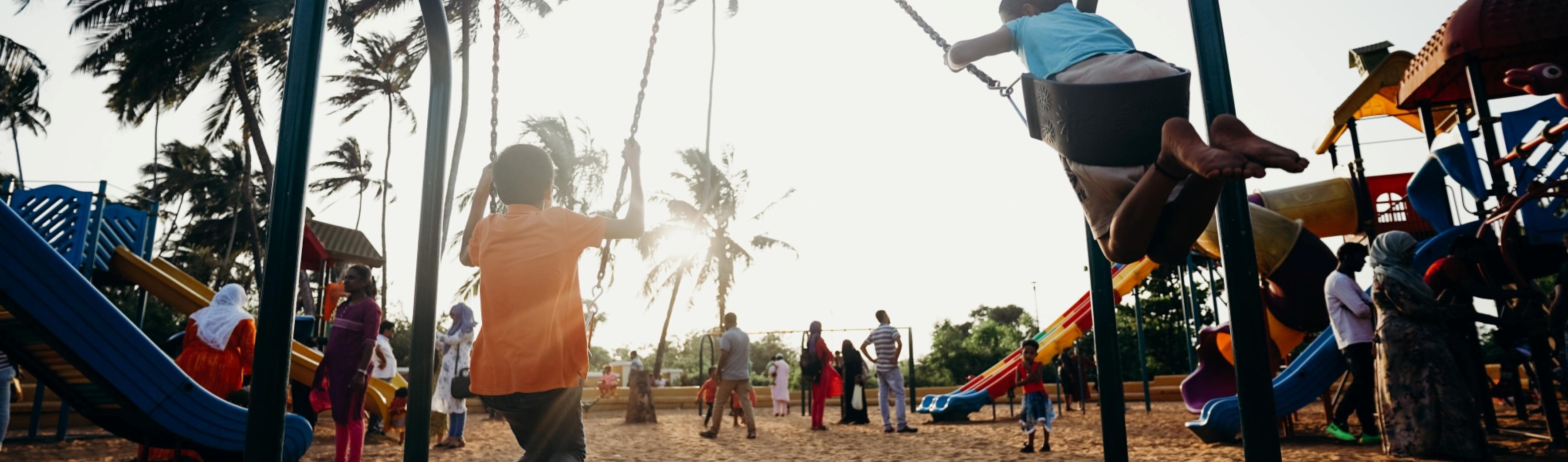 Crianças brincando em balanços em um parque de bairro repleto de árvores